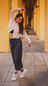 Stylish young woman dancing in a sunny urban arcade, showcasing movement and fashion.