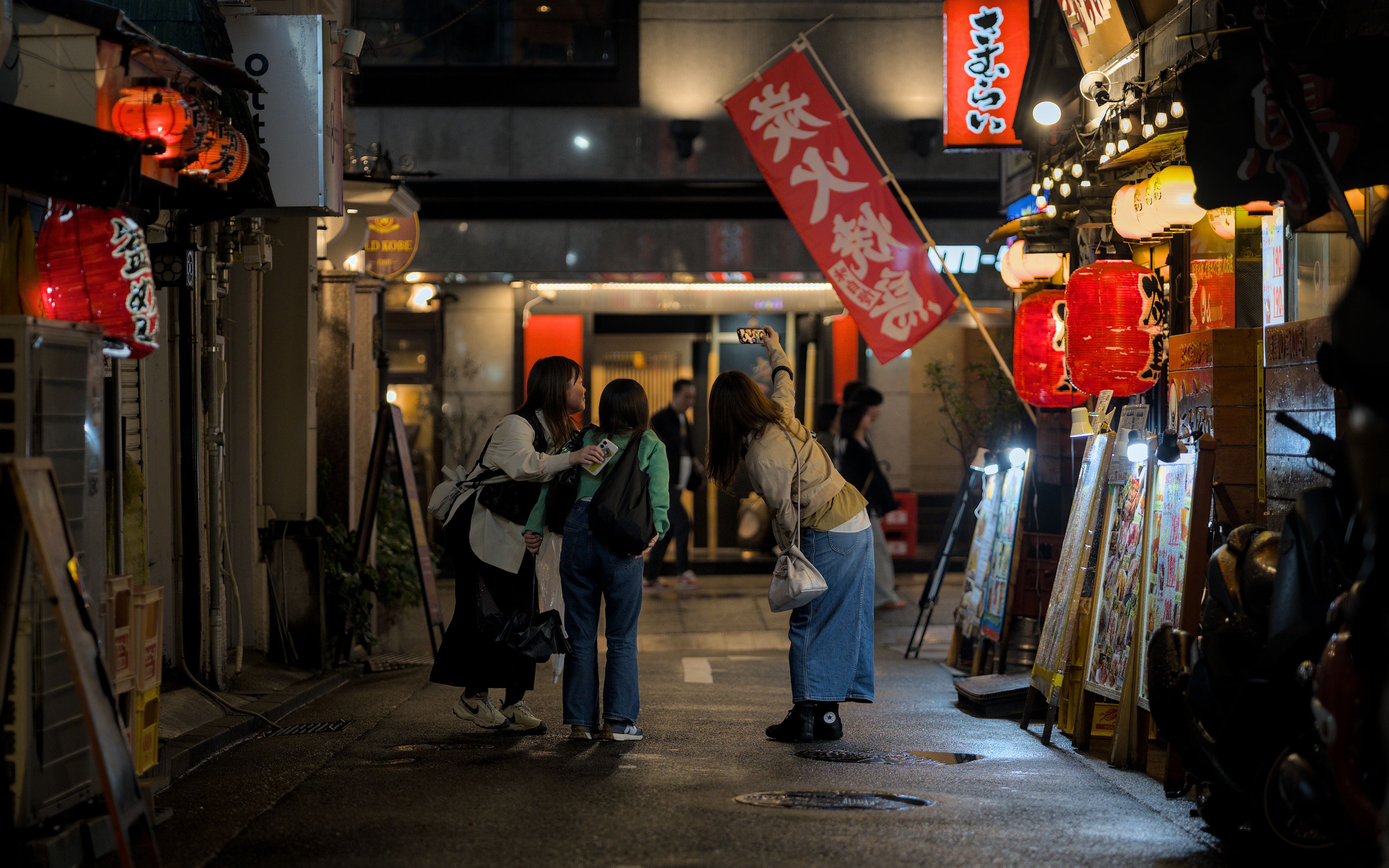 A vibrant scene capturing nightlife in Kobe, Japan with illuminated lanterns and locals enjoying the night.