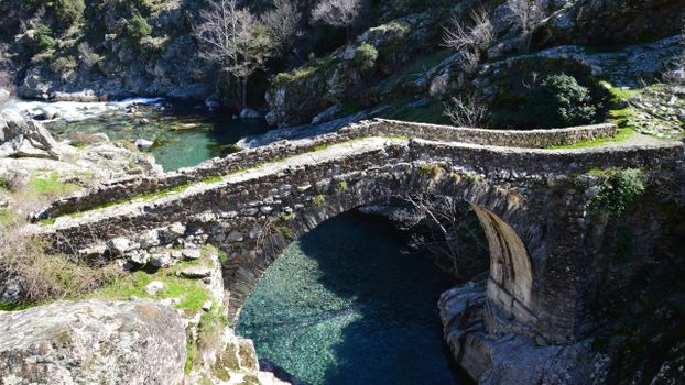 Ancient stone bridge over clear river in picturesque Asco, Corsica, France.
