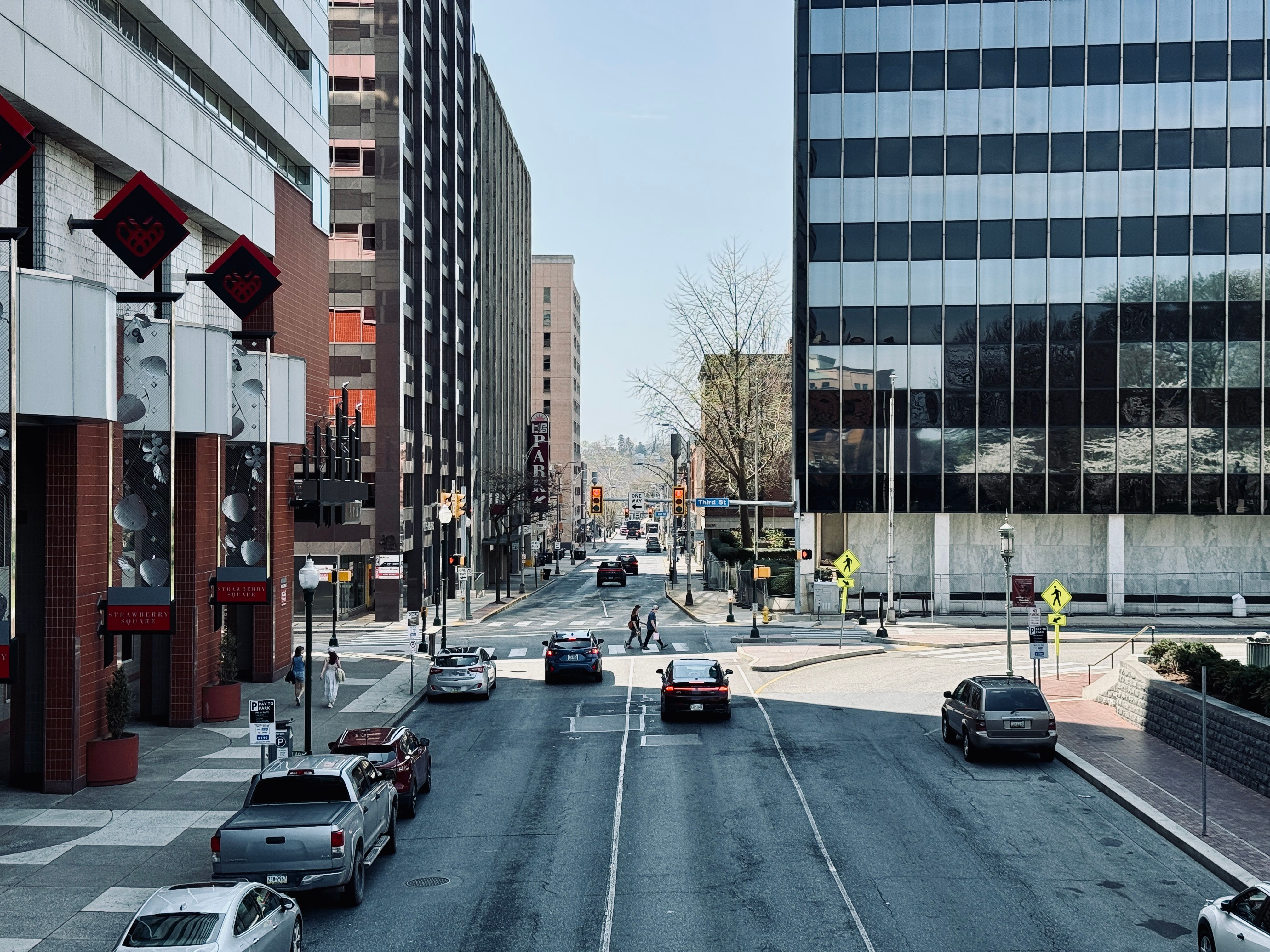 Busy city street scene with cars, pedestrians, and modern buildings.