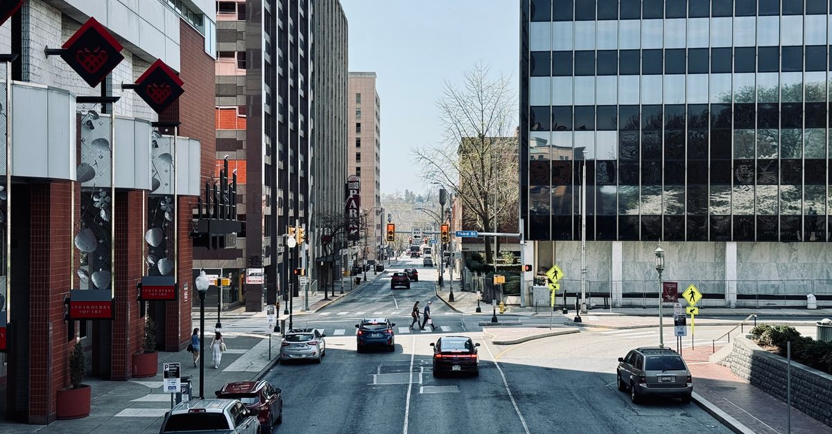 Busy city street scene with cars, pedestrians, and modern buildings.