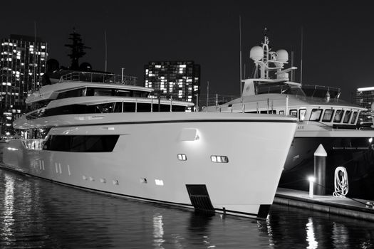 Captivating black and white photo of a luxury yacht docked at a marina with city lights in the background, shot at night.