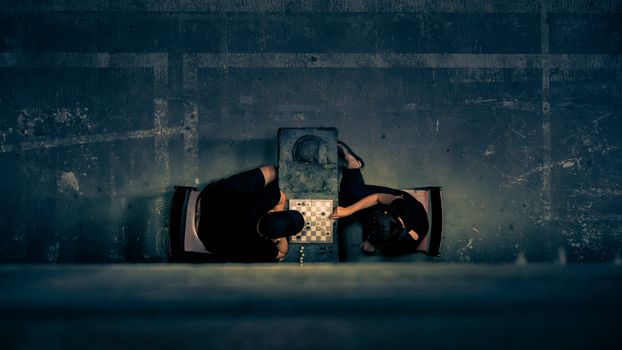 Aerial shot of two people playing chess in a dimly lit, artistic setting.