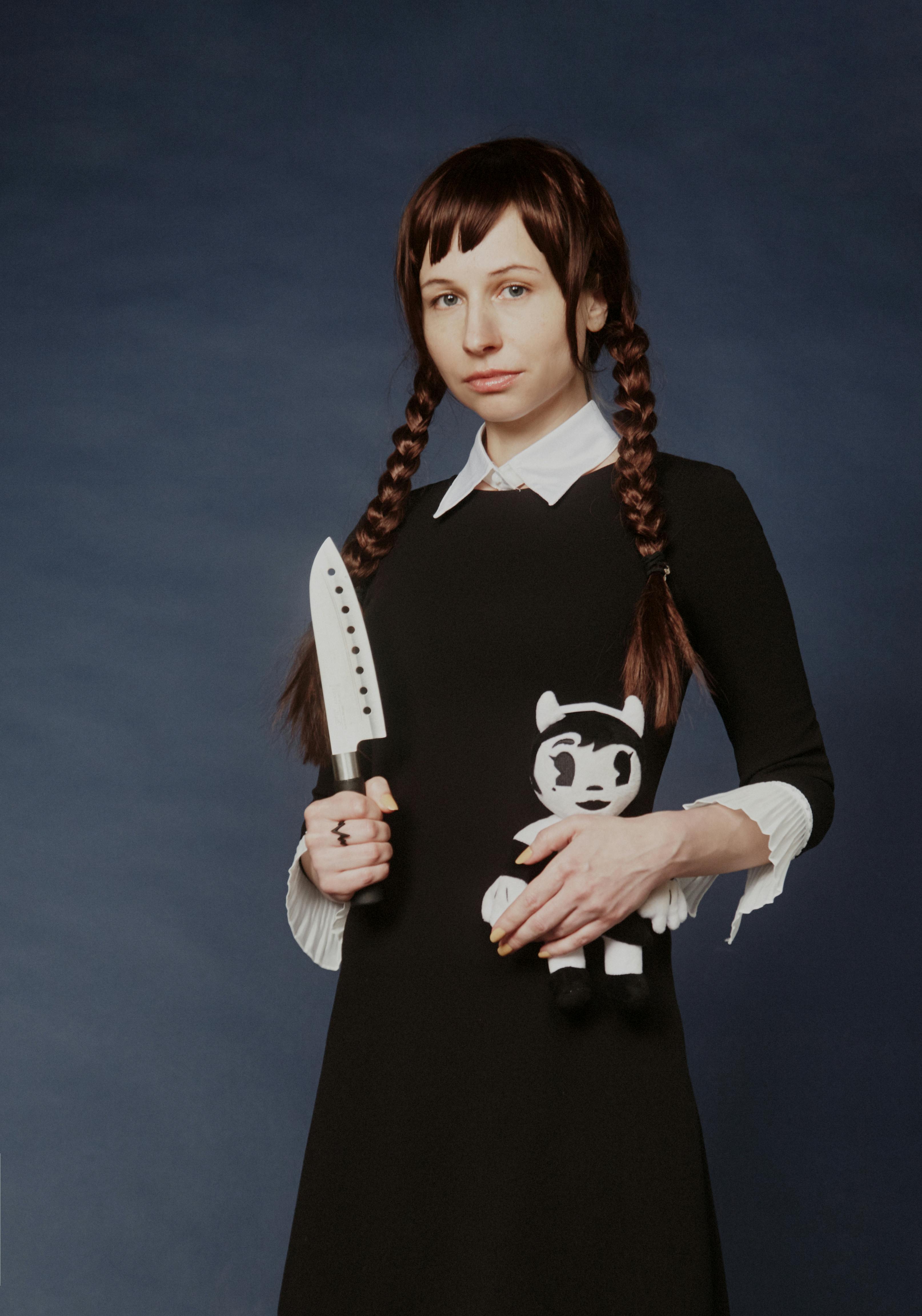 woman wearing black dress while holding a knife and doll