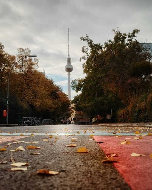 Free Street view of Berlin's iconic TV Tower surrounded by autumn trees under a cloudy sky. Stock Photo