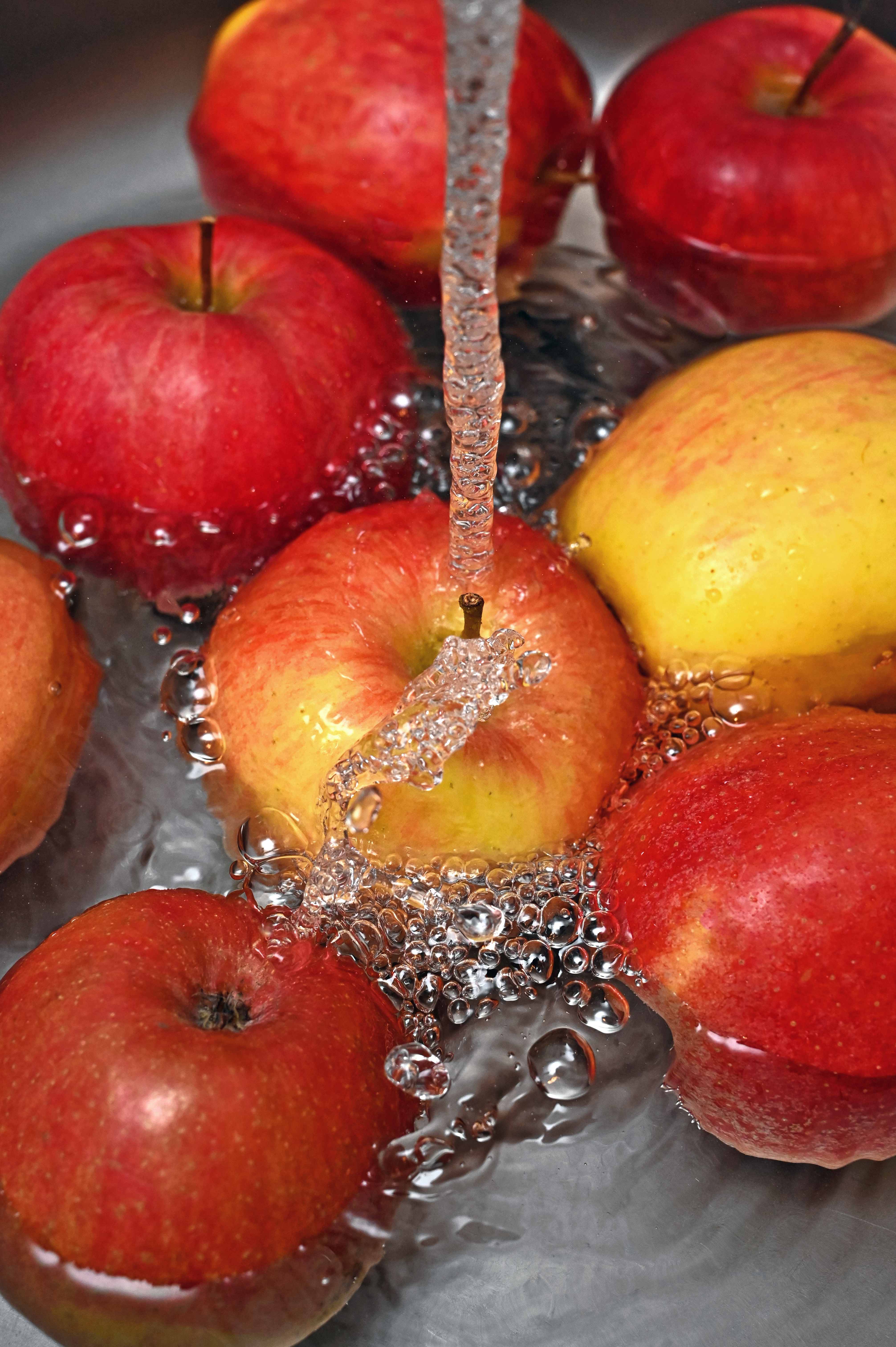 Vibrant red and yellow apples being washed under a stream of water, highlighting freshness.