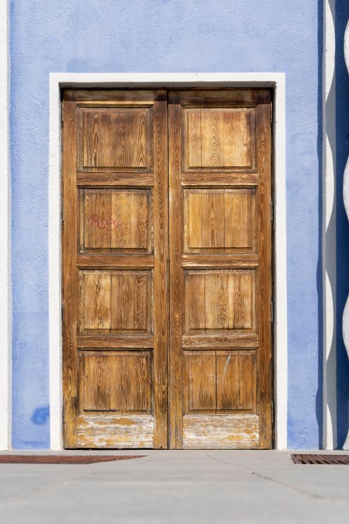 Free A vintage wooden door set against a vibrant blue stucco wall, showcasing rustic charm. Stock Photo