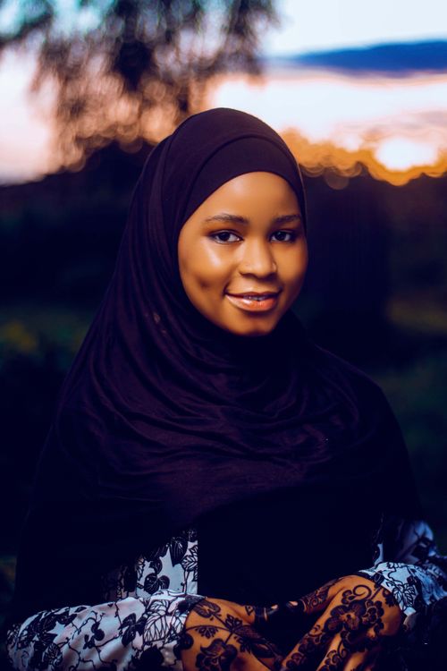 Free Portrait of a smiling woman wearing a hijab with henna-decorated hands during sunset. Stock Photo