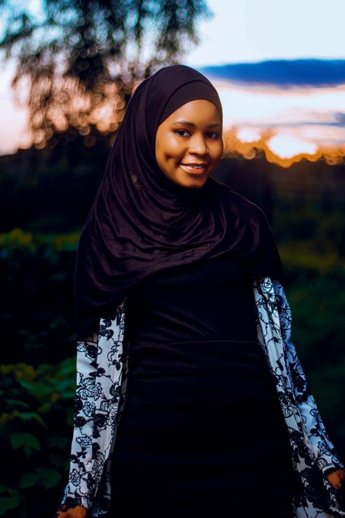 Free Smiling woman wearing black hijab during sunset in a scenic outdoor setting. Vibrant and serene. Stock Photo