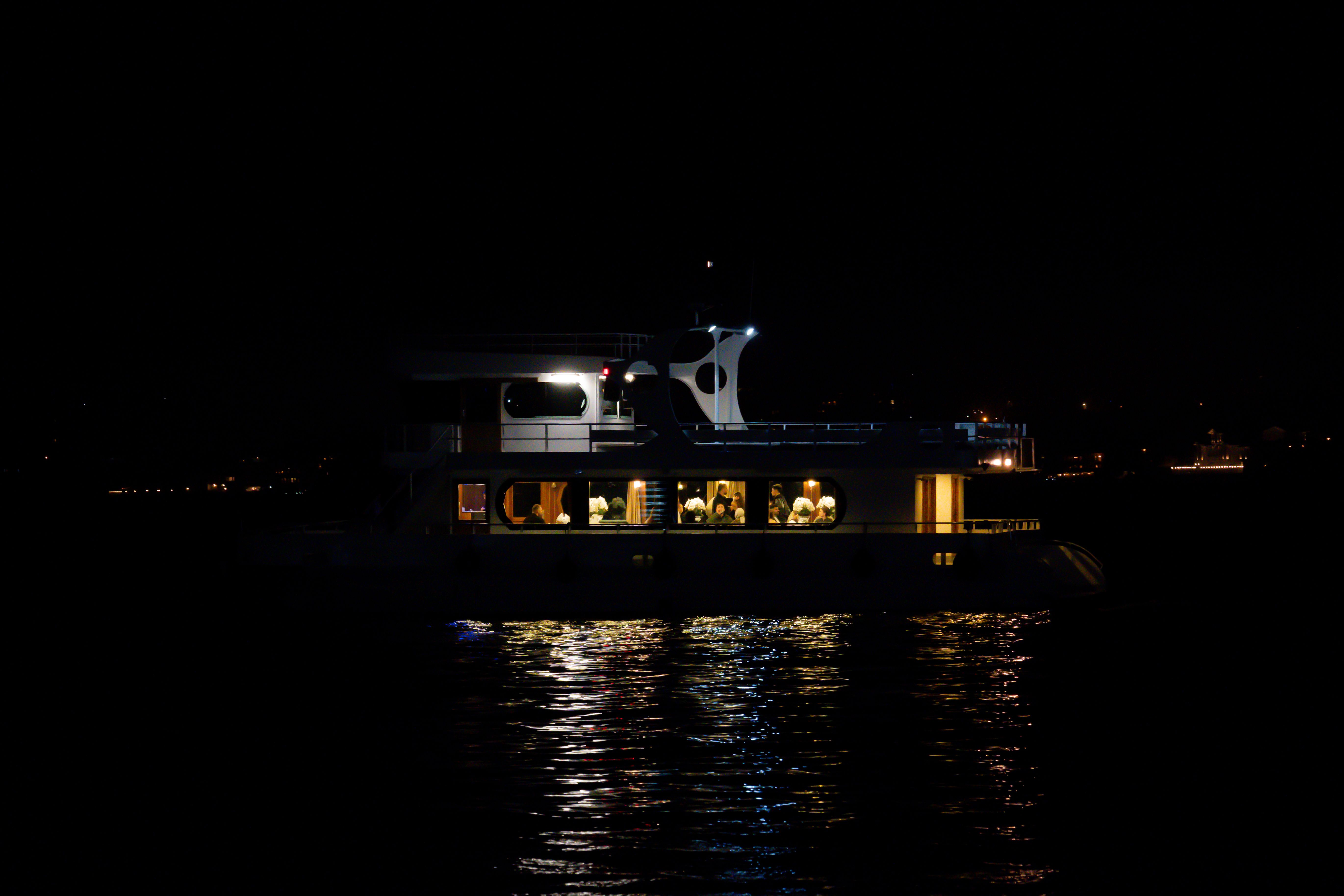Illuminated yacht cruises through İstanbul at night, casting reflections on the water.