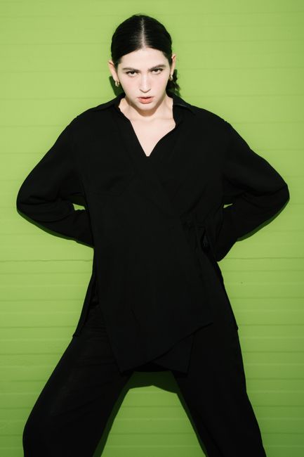 Stylish adult in black attire poses against green background, showcasing modern fashion.