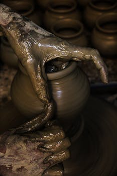 特写镜头中，手将粘土在轮子上塑造成陶器，展示了传统工艺