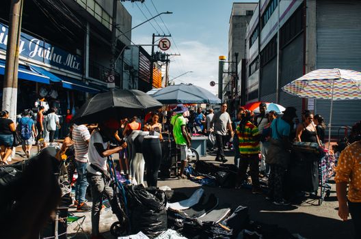 Busy street market with diverse people shopping under umbrellas on a sunny day.