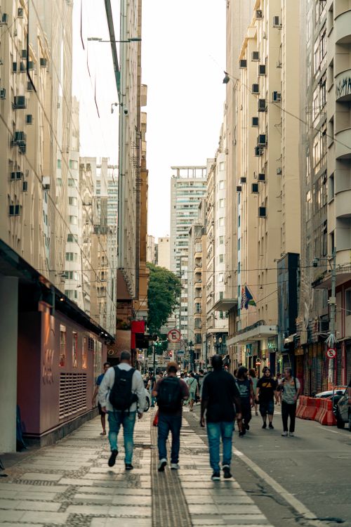 Free A lively city street scene with diverse pedestrians walking between tall buildings. Stock Photo