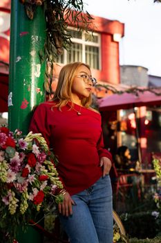 Stylish woman in glasses poses near floral arrangement at an outdoor café.