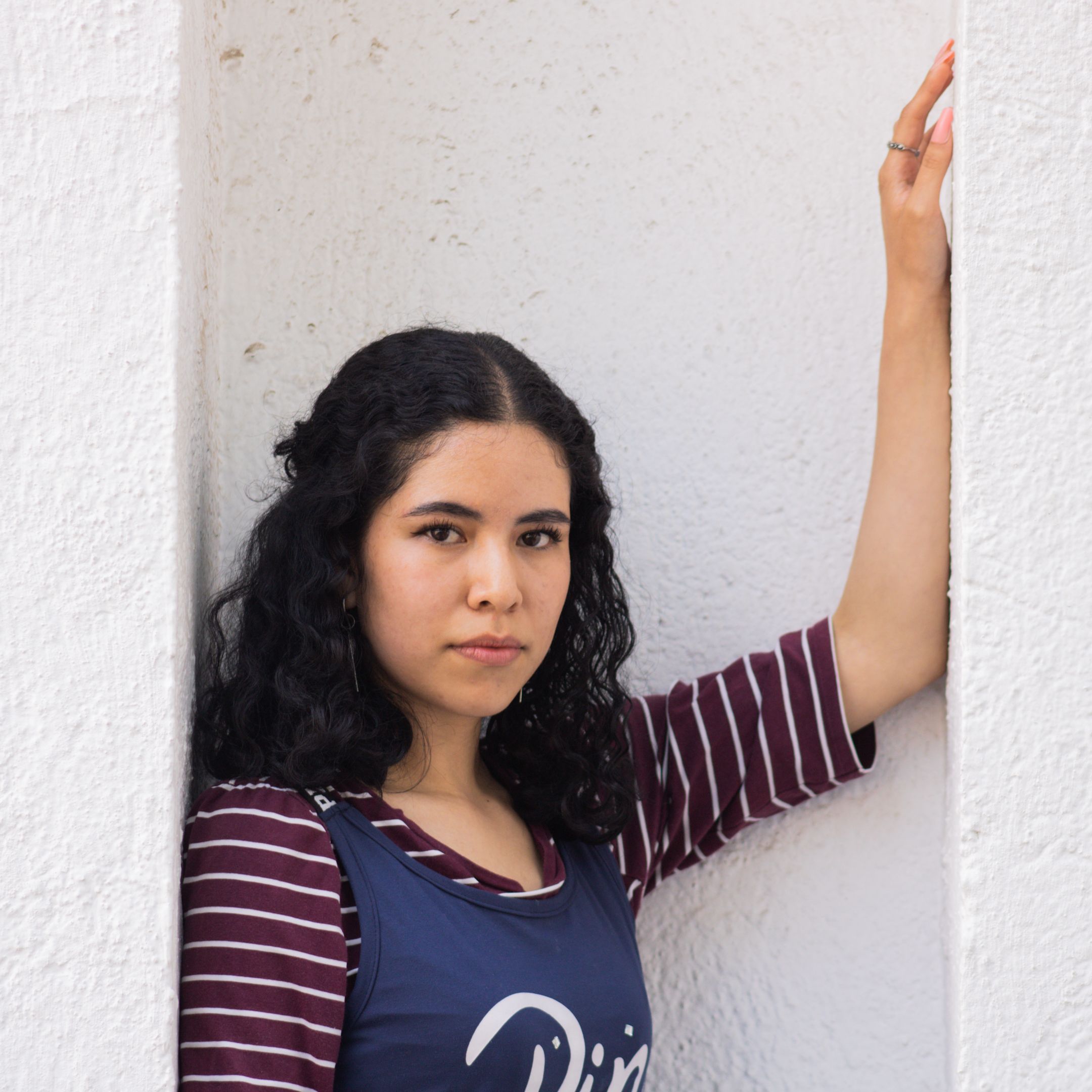 Portrait of a young woman standing by a white wall wearing a striped shirt.
