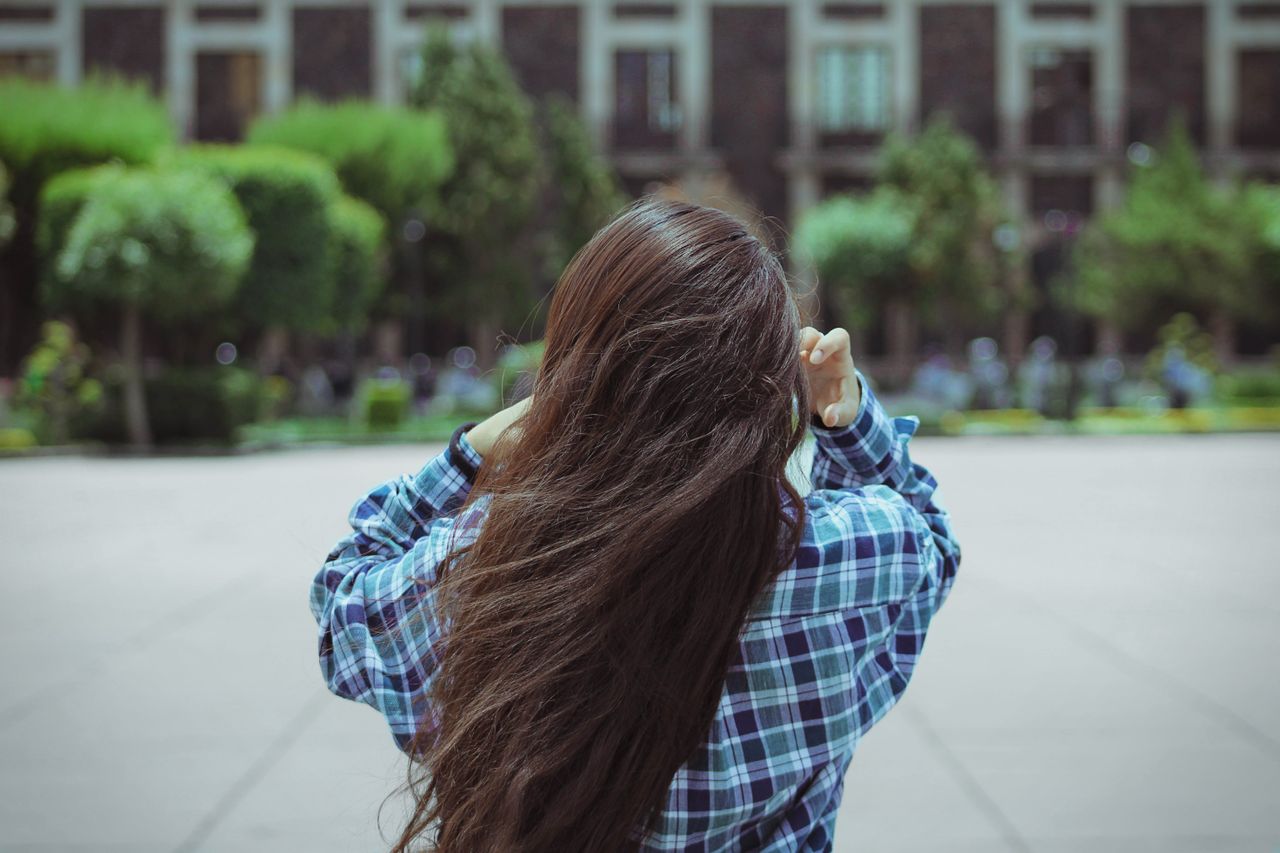 rear view of a young woman with long hair in a checkered shirt adjusti