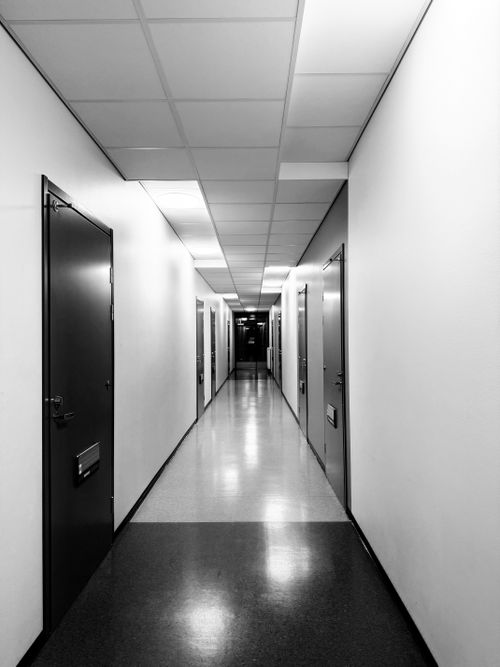 Free Monochrome hallway with overhead lights and closed doors creating a mysterious atmosphere. Stock Photo