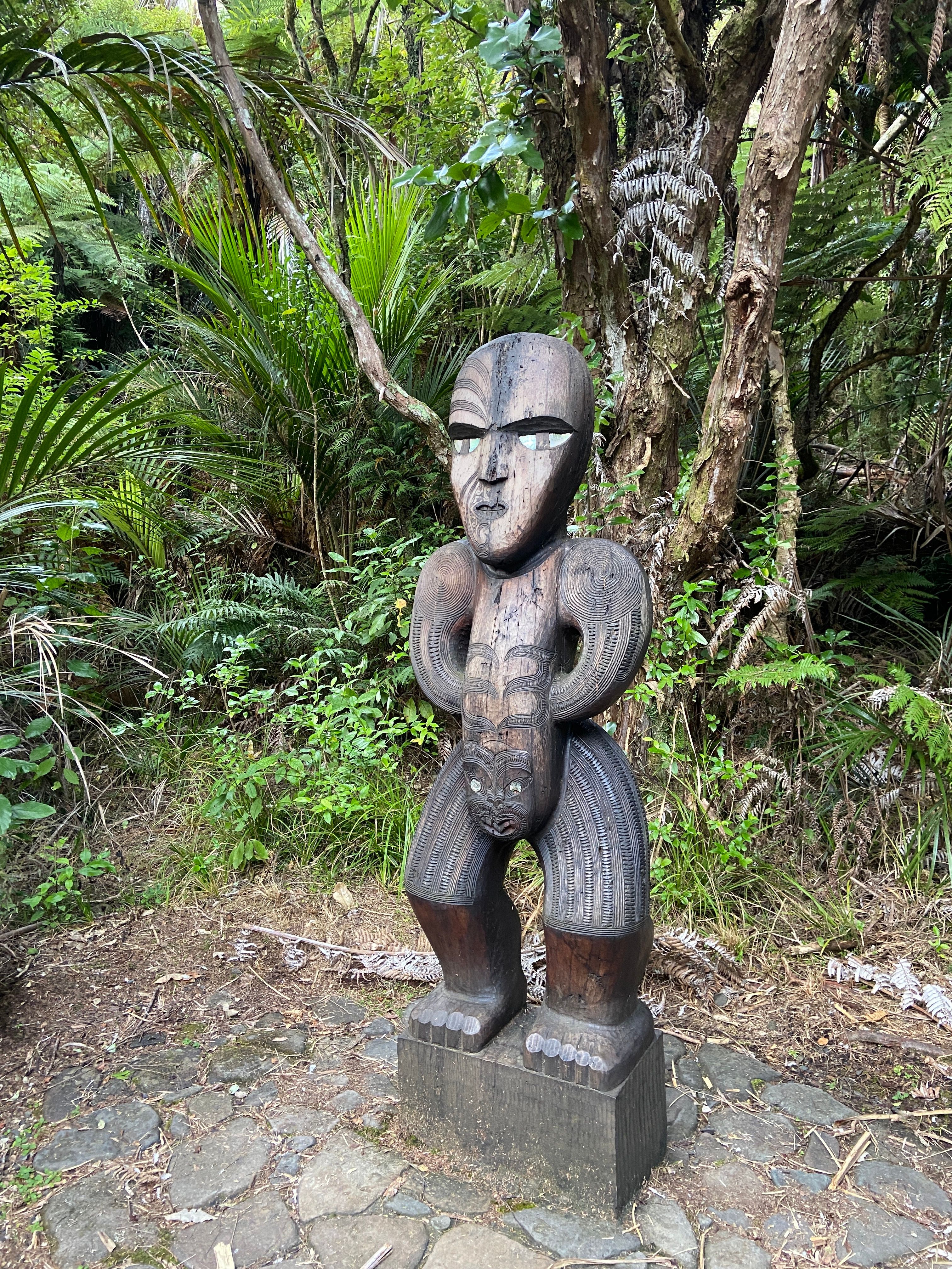 Intricate Maori carved statue amidst lush forest in Auckland, New Zealand.