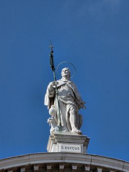 Elegant statue of Saint Roch atop a building in Prague, captured under a clear blue sky.