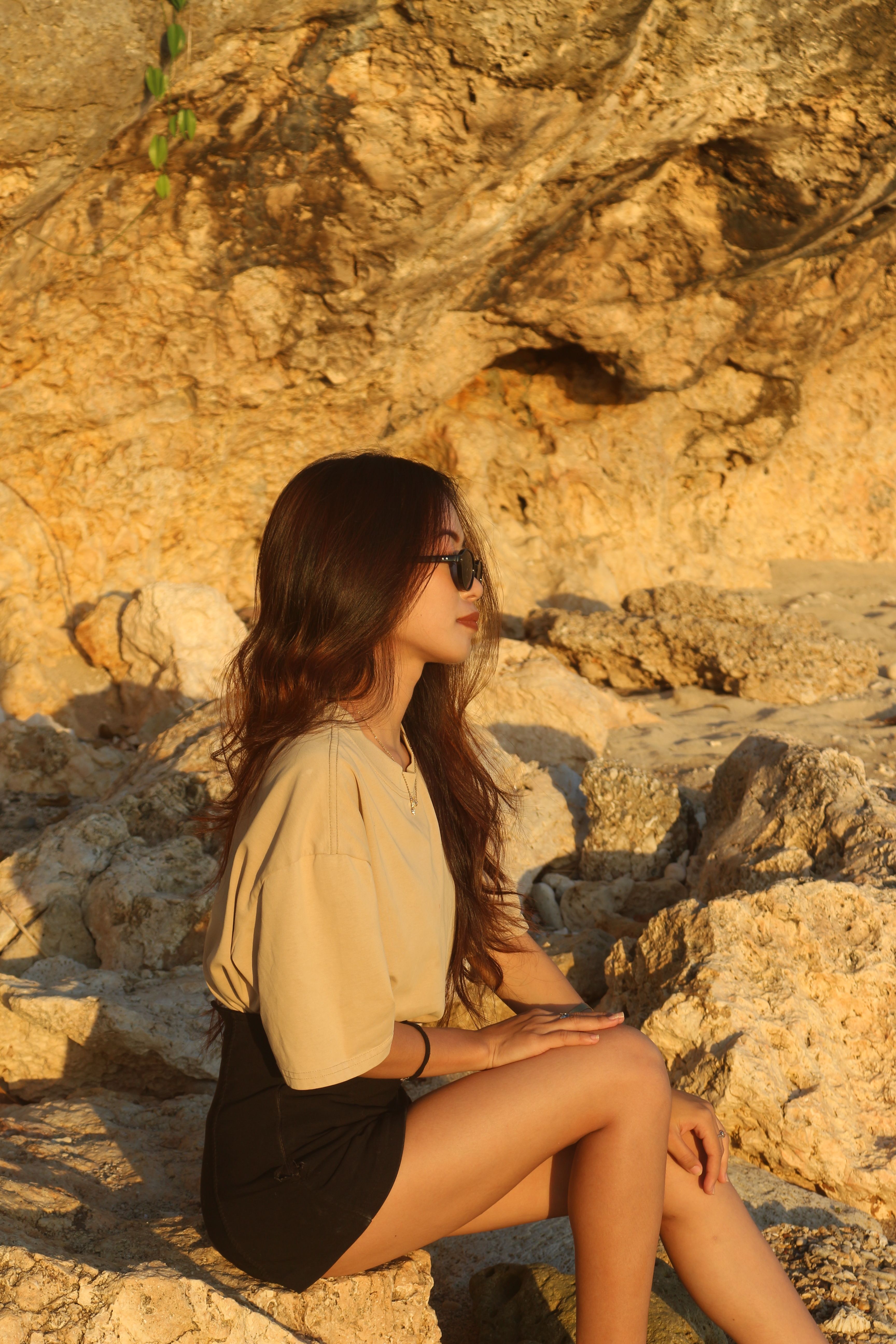 A woman in sunglasses enjoying the summer sun by a rocky coastal landscape.