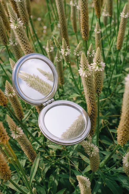 Compact mirror reflecting wildflowers in a lush green field in Ho Chi Minh City.