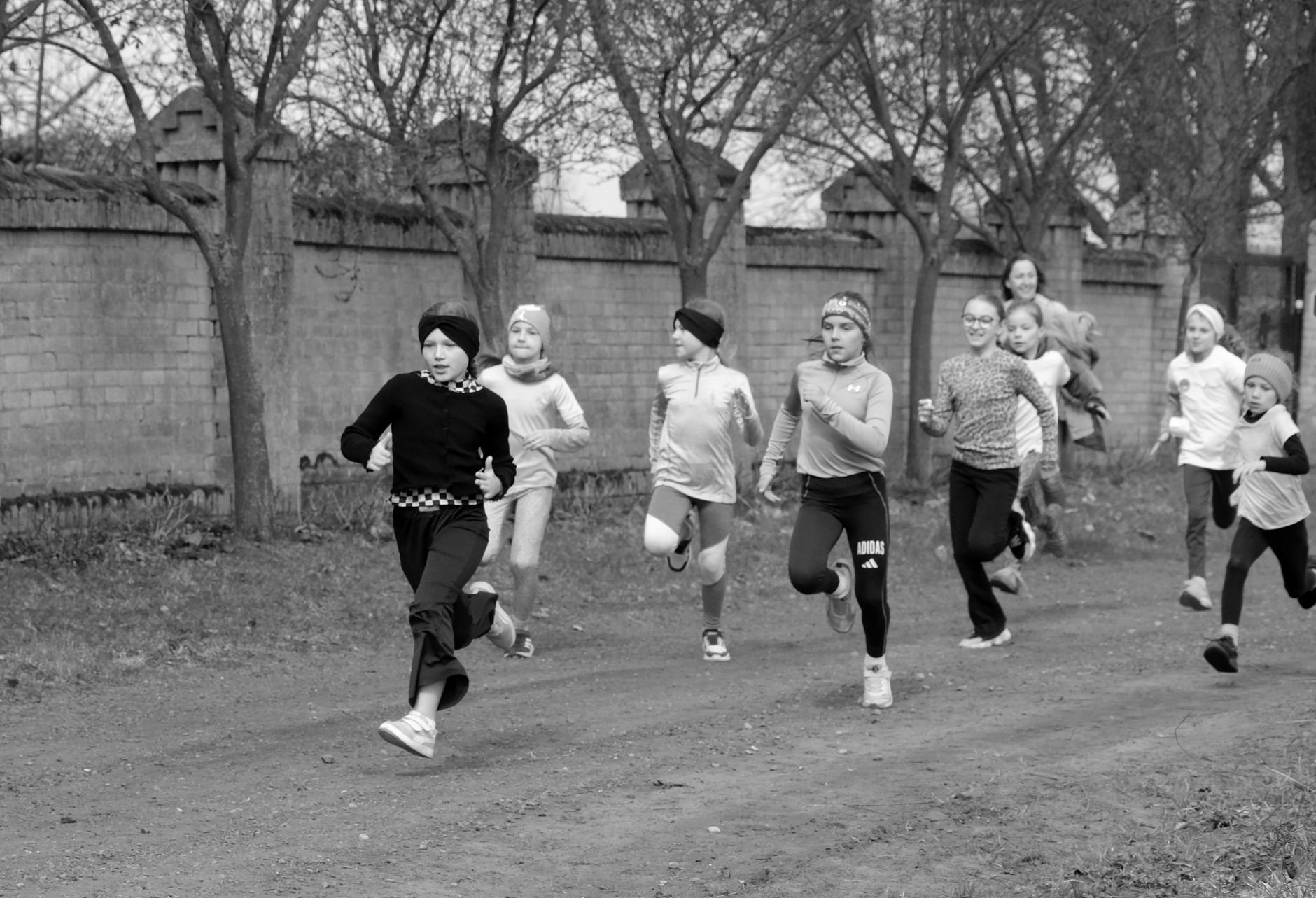 Children energetically running on a track outdoors, captured in black and white.