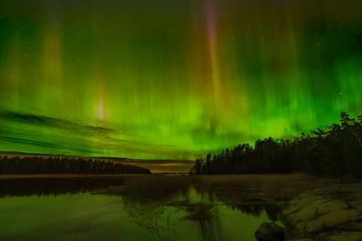 A mesmerizing display of Northern Lights reflecting on a tranquil lake under a starry night sky.
