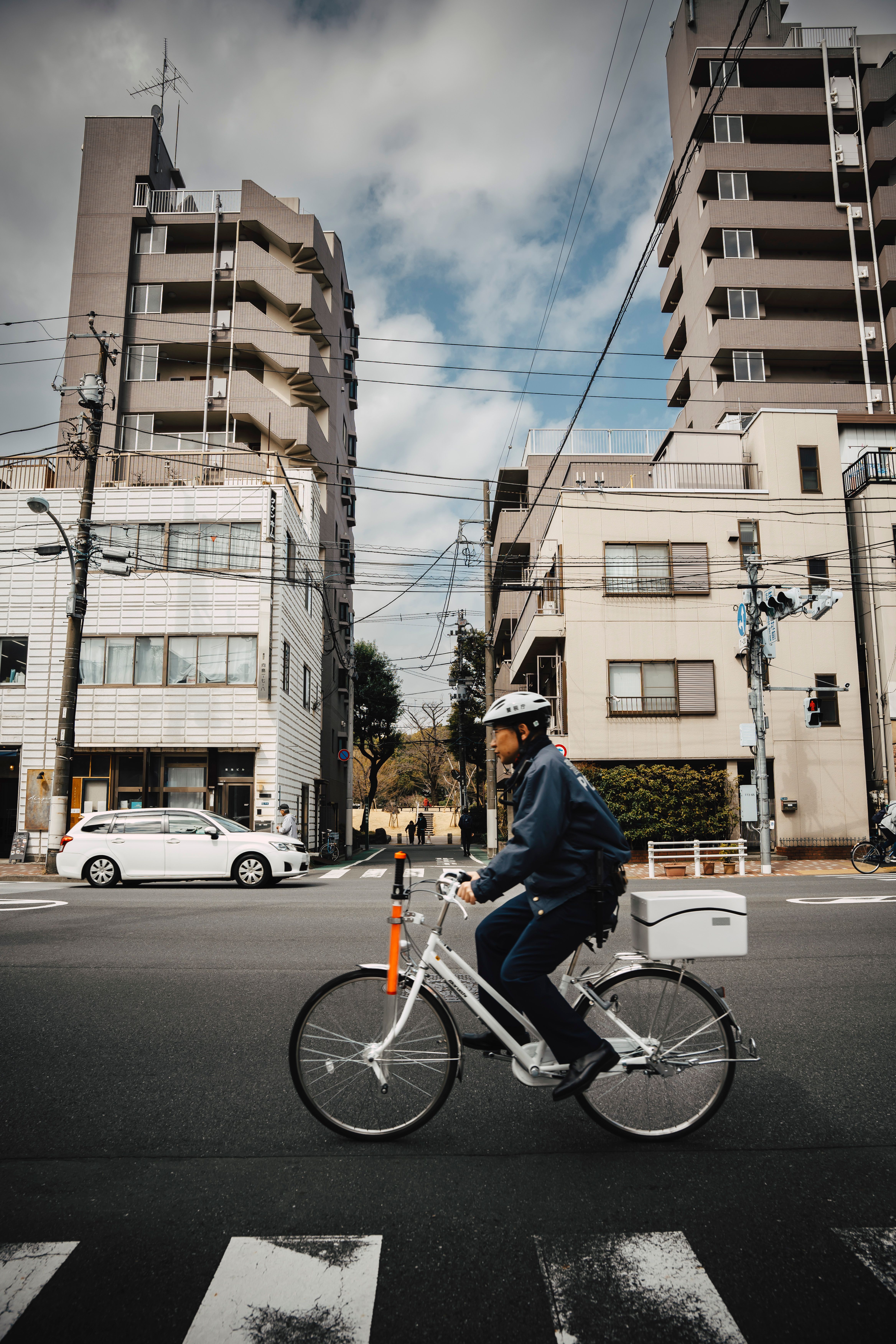 A bicyclist crosses an intersection in Tokyo with tall residential buildings in the background.
