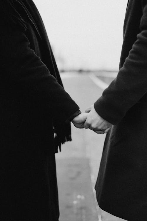 бесплатная Фотография в оттенках серого: пара в черном пальто, взявшись за руки Стоковое фото