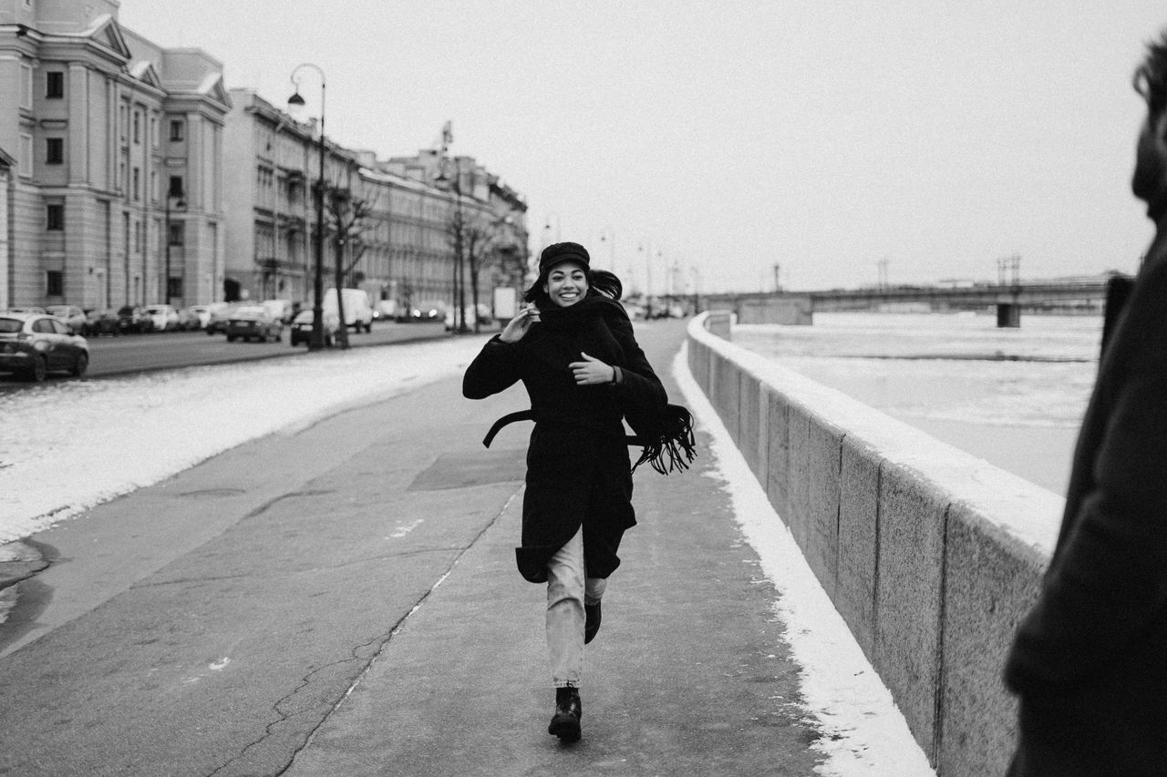 Black and white photo of a woman running along a snowy riverside embankment