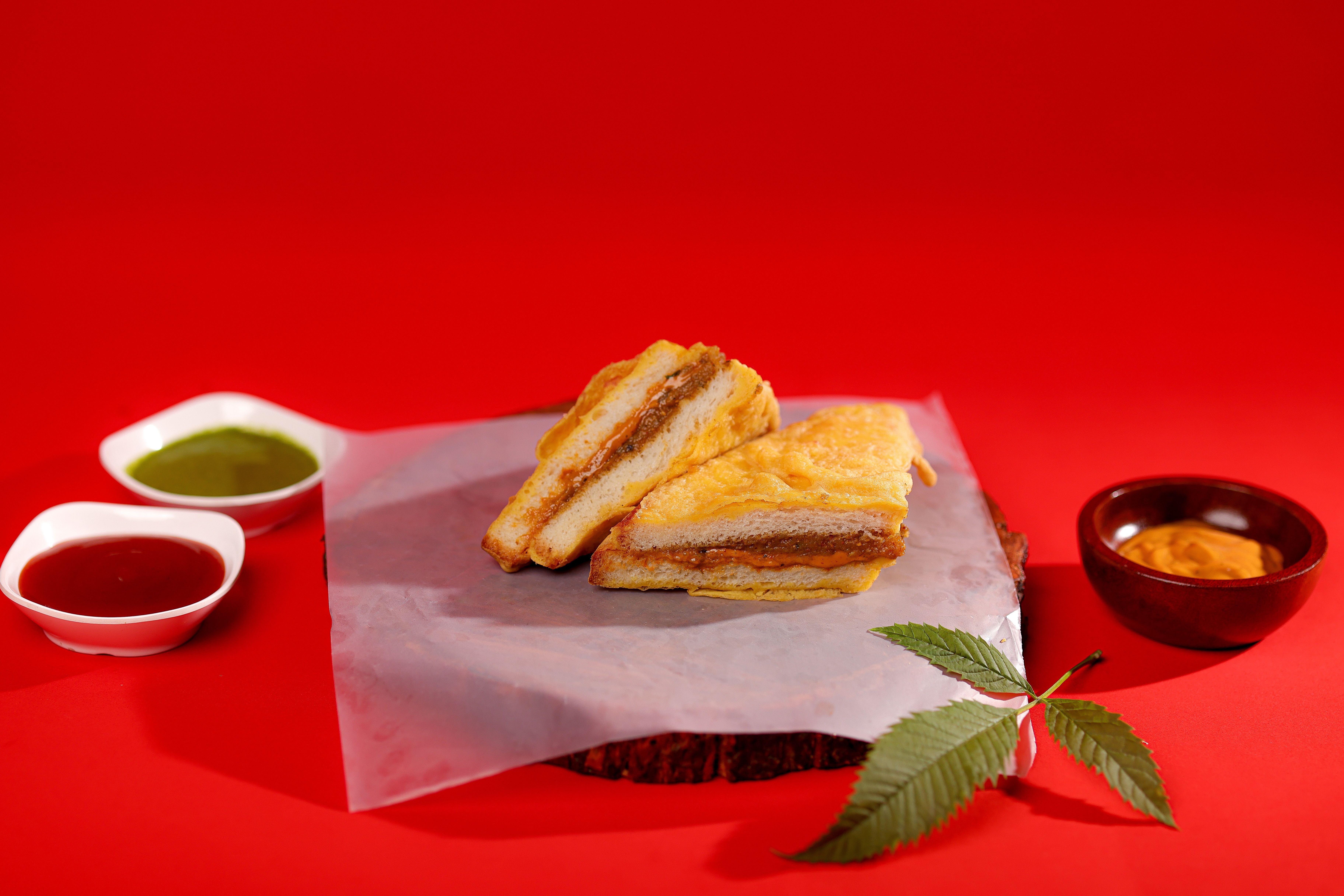 Delicious Indian sandwich with chutneys on vibrant red background.