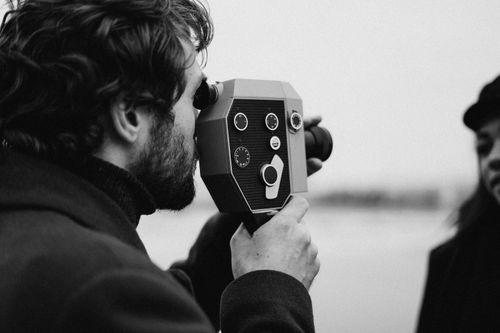 Free A black and white photo of a man with a retro video camera filming a woman outdoors. Stock Photo