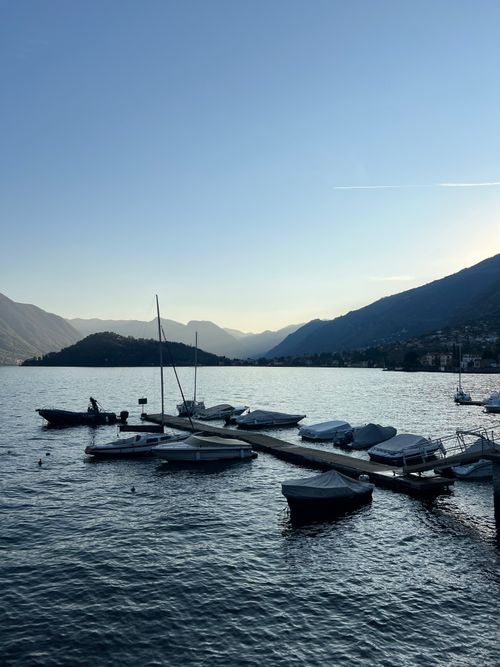 Free Tranquil lake scene with boats docked and mountains in the background during sunset. Stock Photo