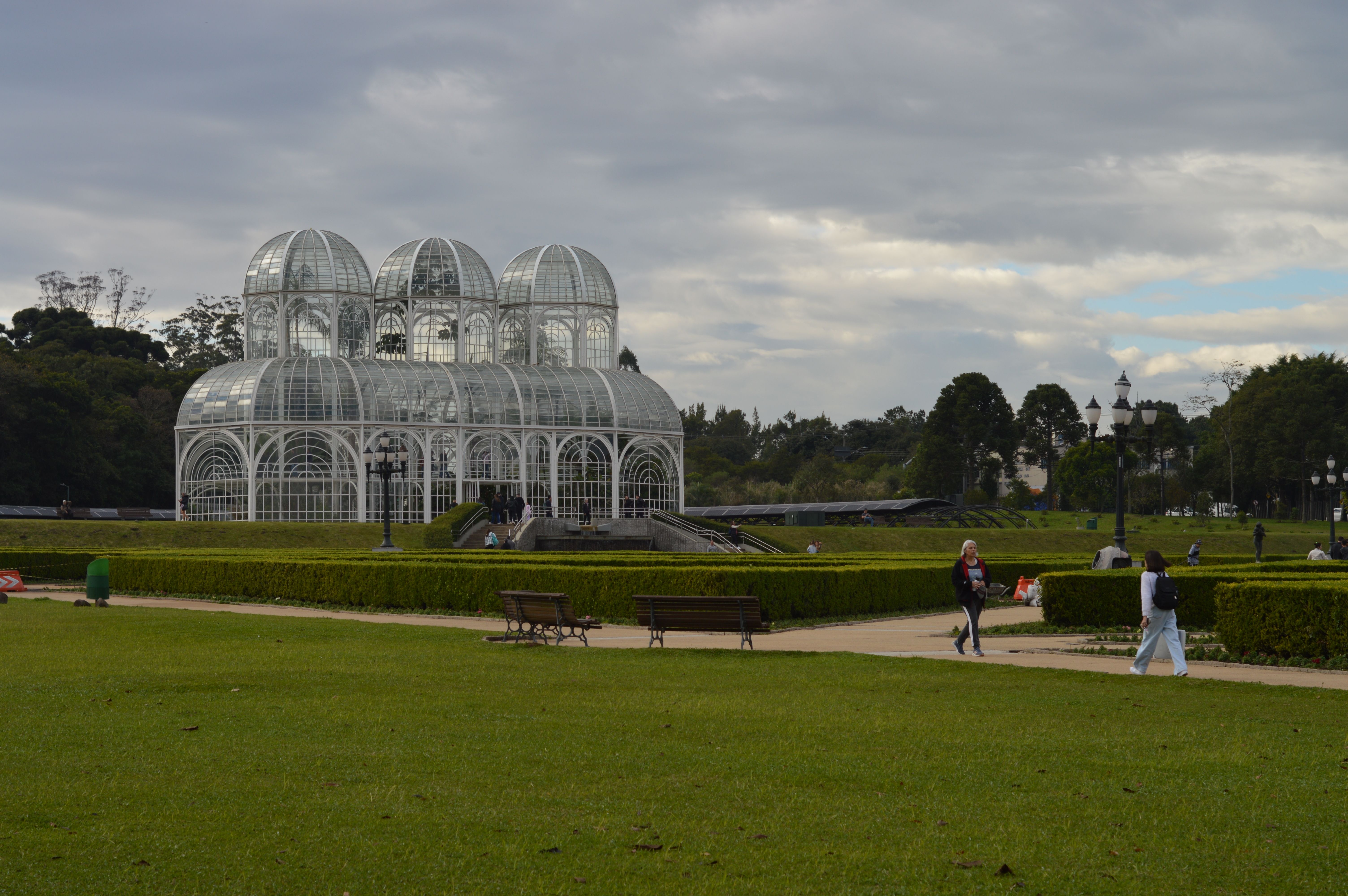Scenic view of the Botanical Garden in Curitiba, featuring the iconic glass greenhouse under a cloudy sky.