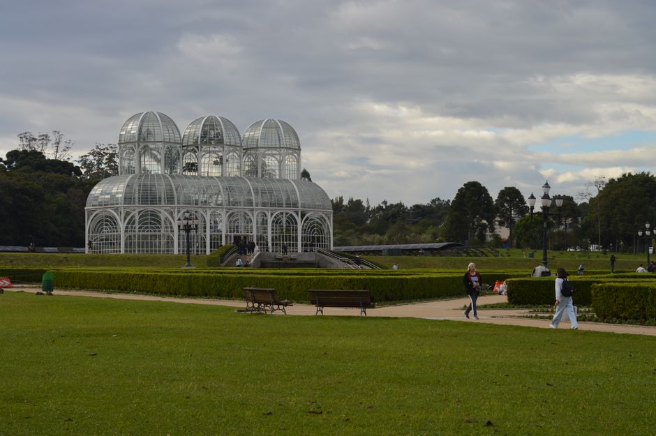 Scenic view of the Botanical Garden in Curitiba, featuring the iconic glass greenhouse under a cloudy sky.