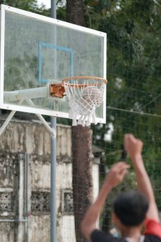A basketball game captured with focus on the hoop and player celebrating.