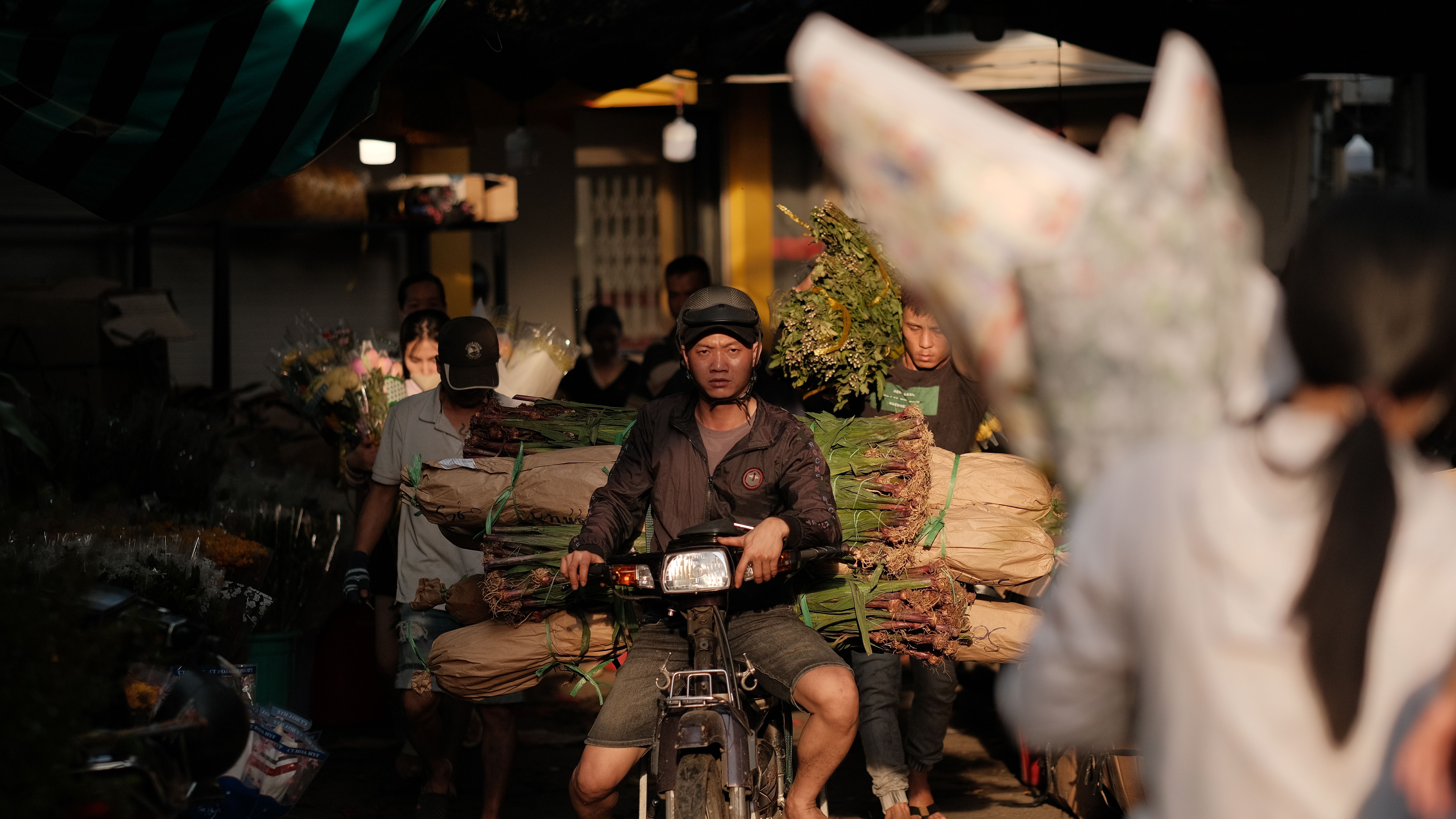 A man on a motorcycle transports flowers in a lively market setting.