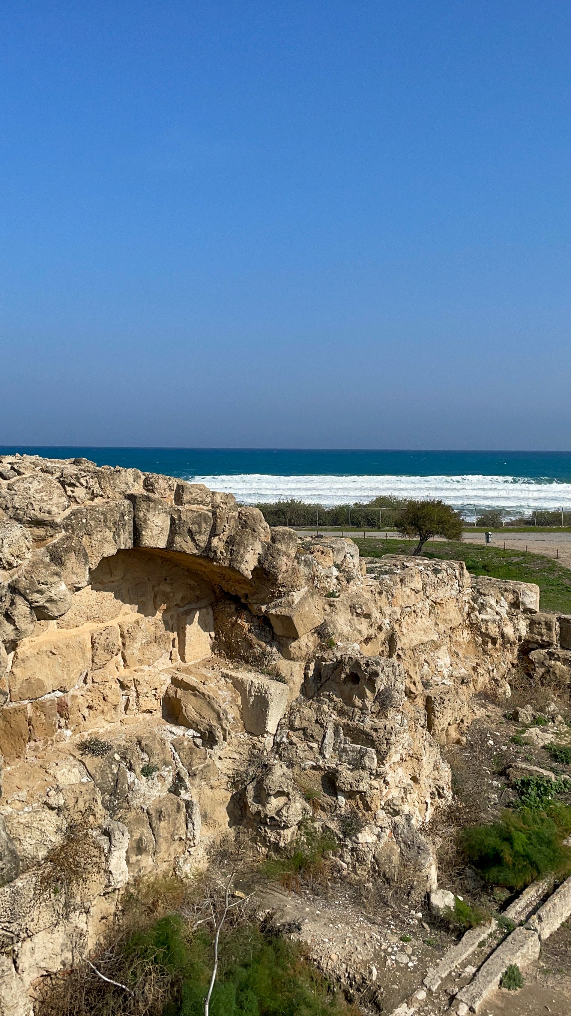 Stone ruins with ocean vista under blue sky, capturing historical charm and natural beauty.