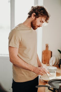 A man prepares breakfast in a bright kitchen, mixing ingredients with care.