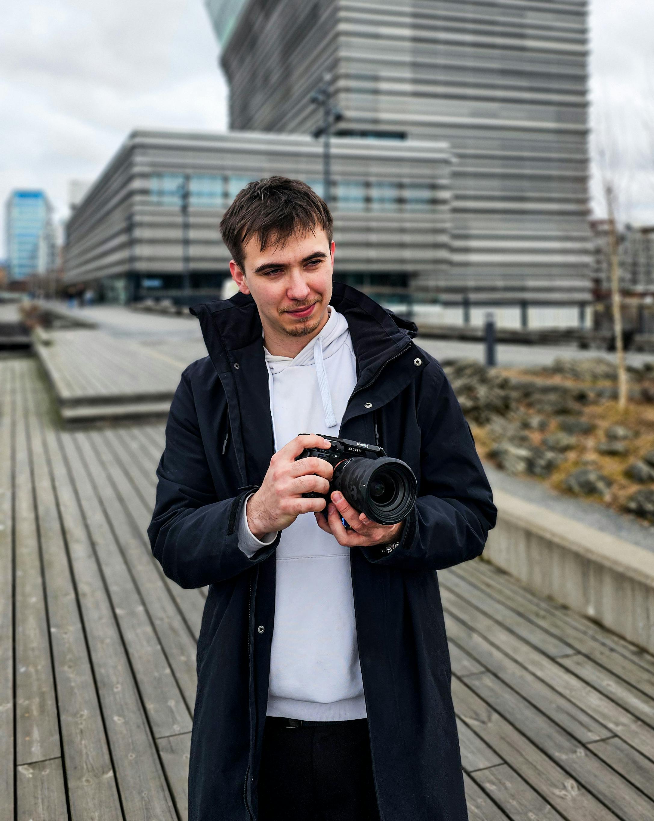 Young photographer holding a camera in an urban outdoor setting.