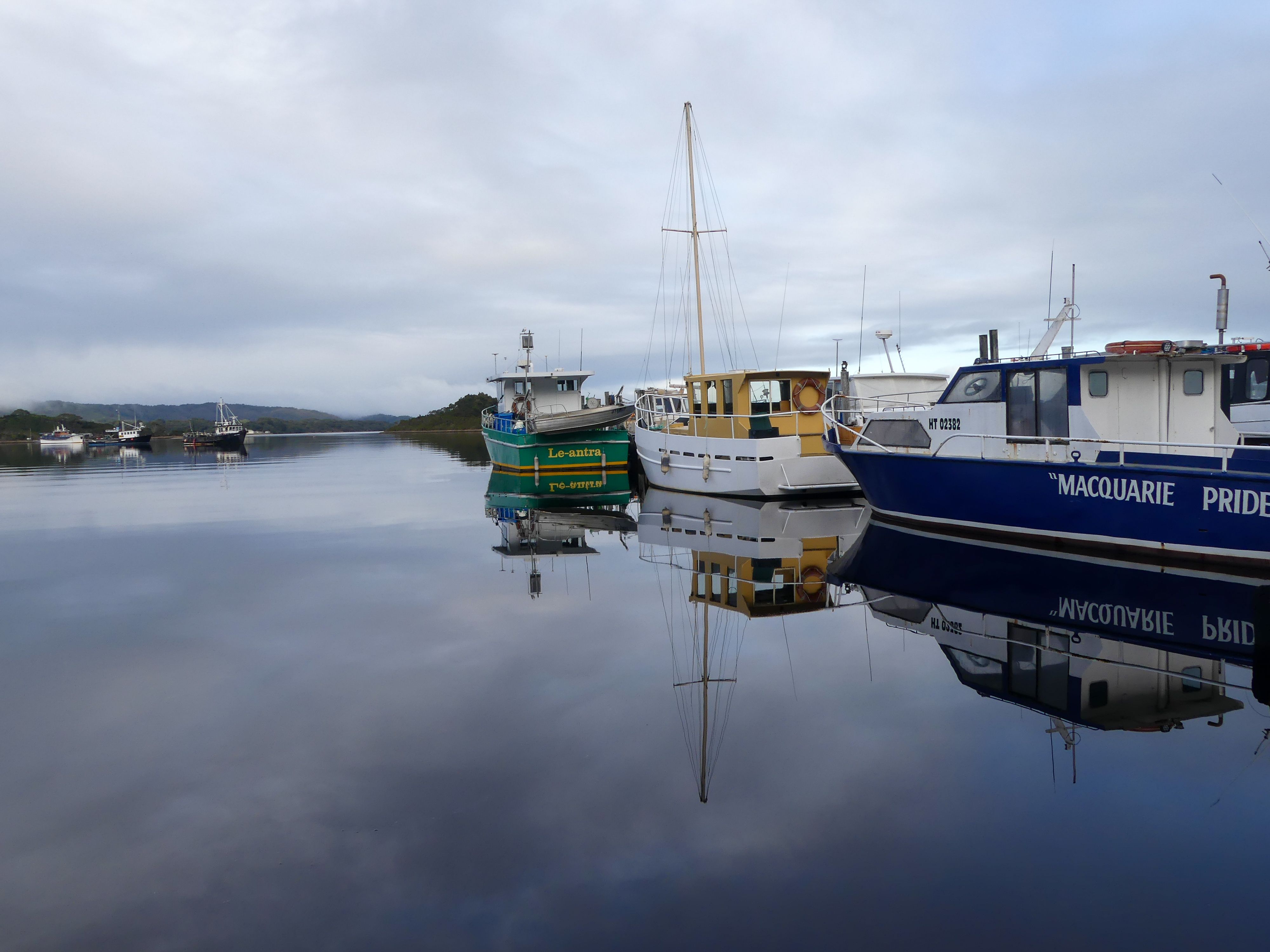 Peaceful scene of boats reflecting in Macquarie Harbour, Tasmania's calm waters.