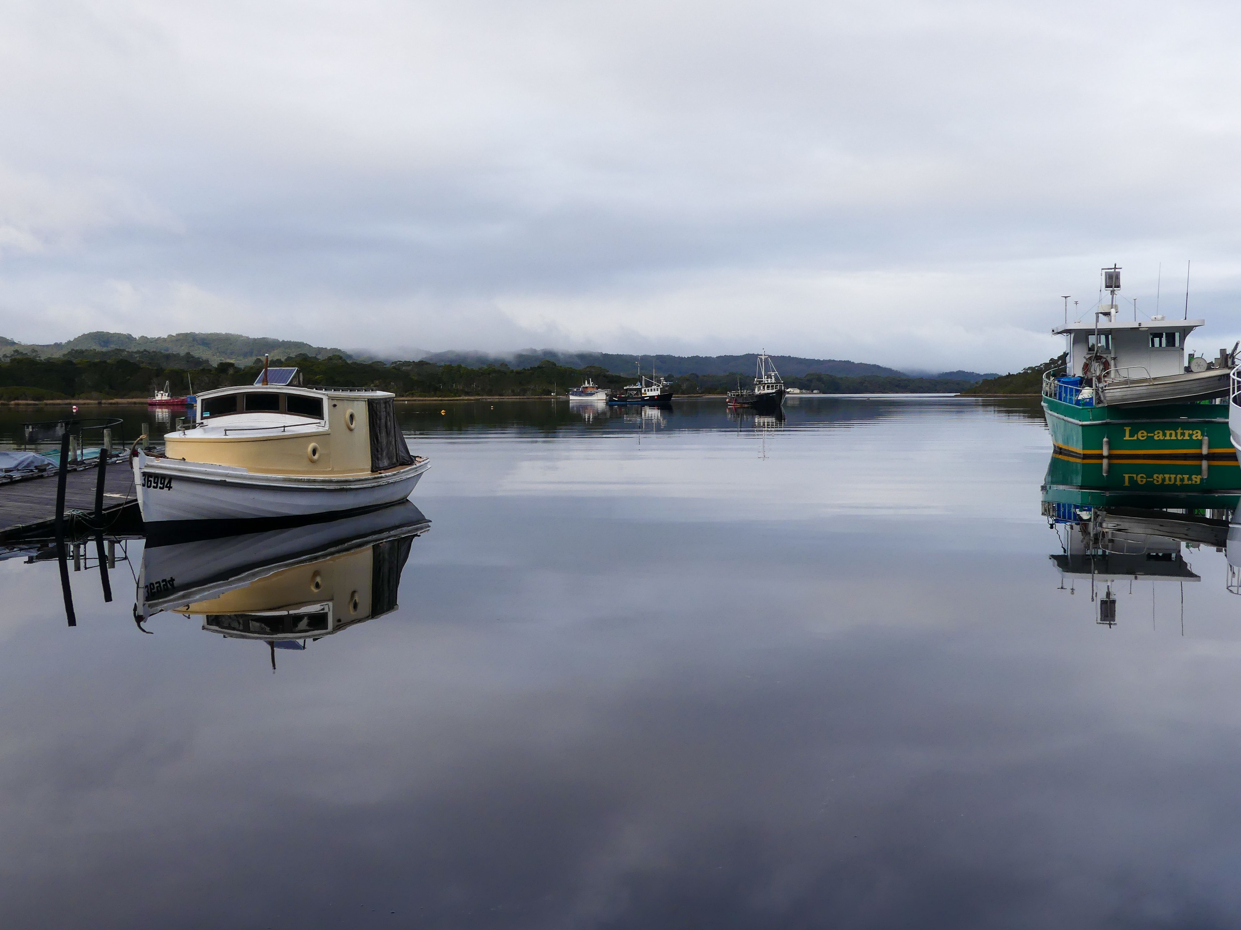 Calm waters reflecting boats on a tranquil Tasmania harbor, ideal for peaceful nature escape.
