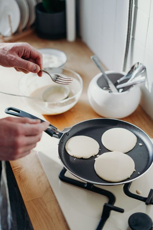 Free Close-up of pancakes cooking in a pan on a gas stove with utensils nearby. Stock Photo