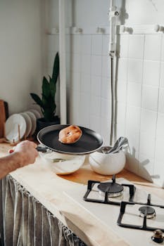 A person cooking pancakes on a stove in a bright kitchen, capturing a homey morning vibe.
