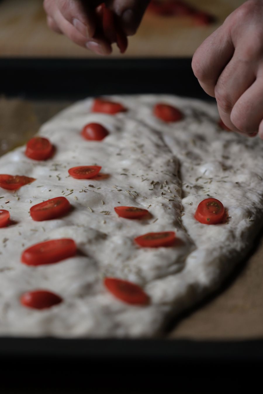 Hands dimpling focaccia dough with herbs and tomatoes — photo by Christina & Peter on Pexels