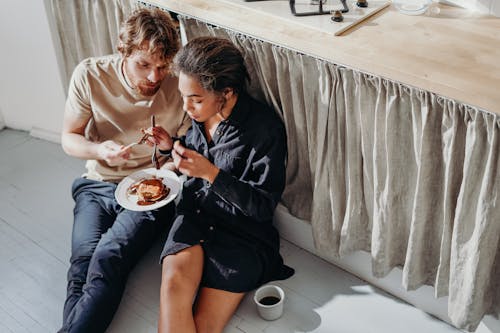 Free Man and Woman Eating Under Kitchen Table Stock Photo