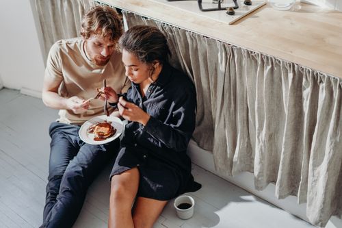Free A couple enjoys a cozy morning breakfast with pancakes and coffee, sitting together on the kitchen floor. Stock Photo