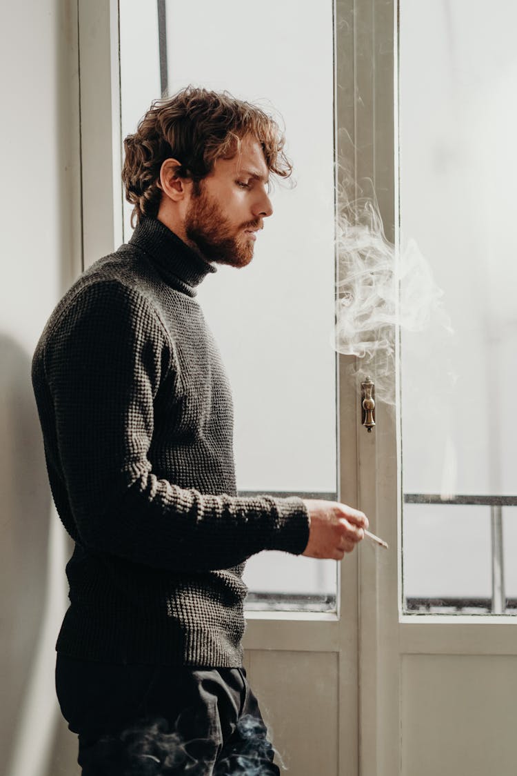 Side View Photo Of Man In Black Sweater Standing Beside White Wooden Door Smoking