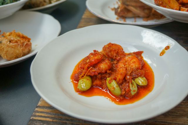 Delicious spicy shrimp dish with green vegetables in a rich, red sauce served on a white plate.